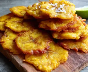 Crispy golden tostones made from fried sliced green plantains on a wooden platter.